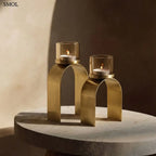 Arany mécsestartó szett két különböző méretű, íves sárgaréz tartóval és borostyánszínű üveggel, asztalon