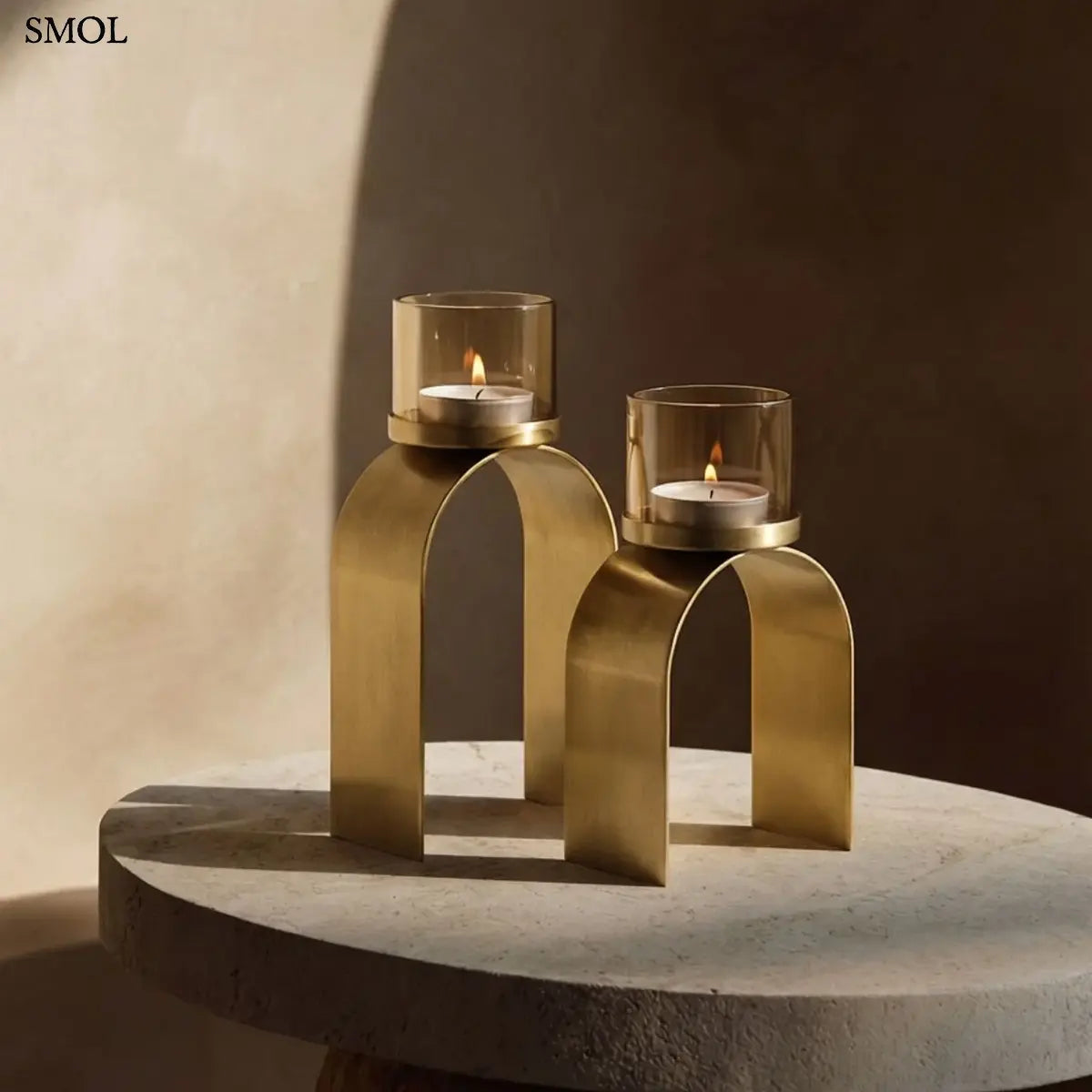 Arany mécsestartó szett két különböző méretű, íves sárgaréz tartóval és borostyánszínű üveggel, asztalon