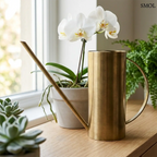 Elegáns sárgaréz öntözőkanna hosszú, vékony kiöntővel és íves fogantyúval, orchideával