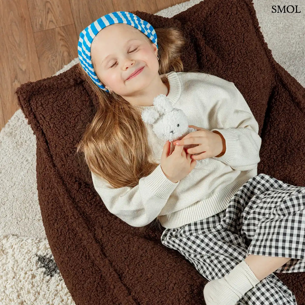 Prémium mogyoróbarna teddy anyagú babzsákfotel gyerekeknek, praktikus fogantyúval és kényelmes, stabil háttámlával, becsukott szemű kisgyerekkel