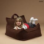 Prémium mogyoróbarna teddy anyagú babzsákfotel gyerekeknek, praktikus fogantyúval és kényelmes, stabil háttámlával, hasaló kisgyerekkel