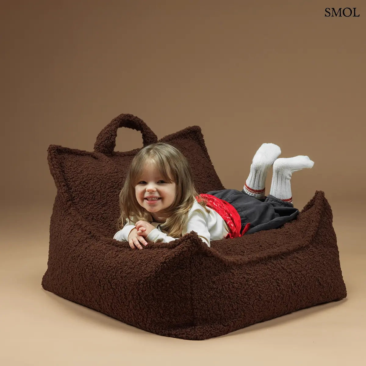 Prémium mogyoróbarna teddy anyagú babzsákfotel gyerekeknek, praktikus fogantyúval és kényelmes, stabil háttámlával, hasaló kisgyerekkel
