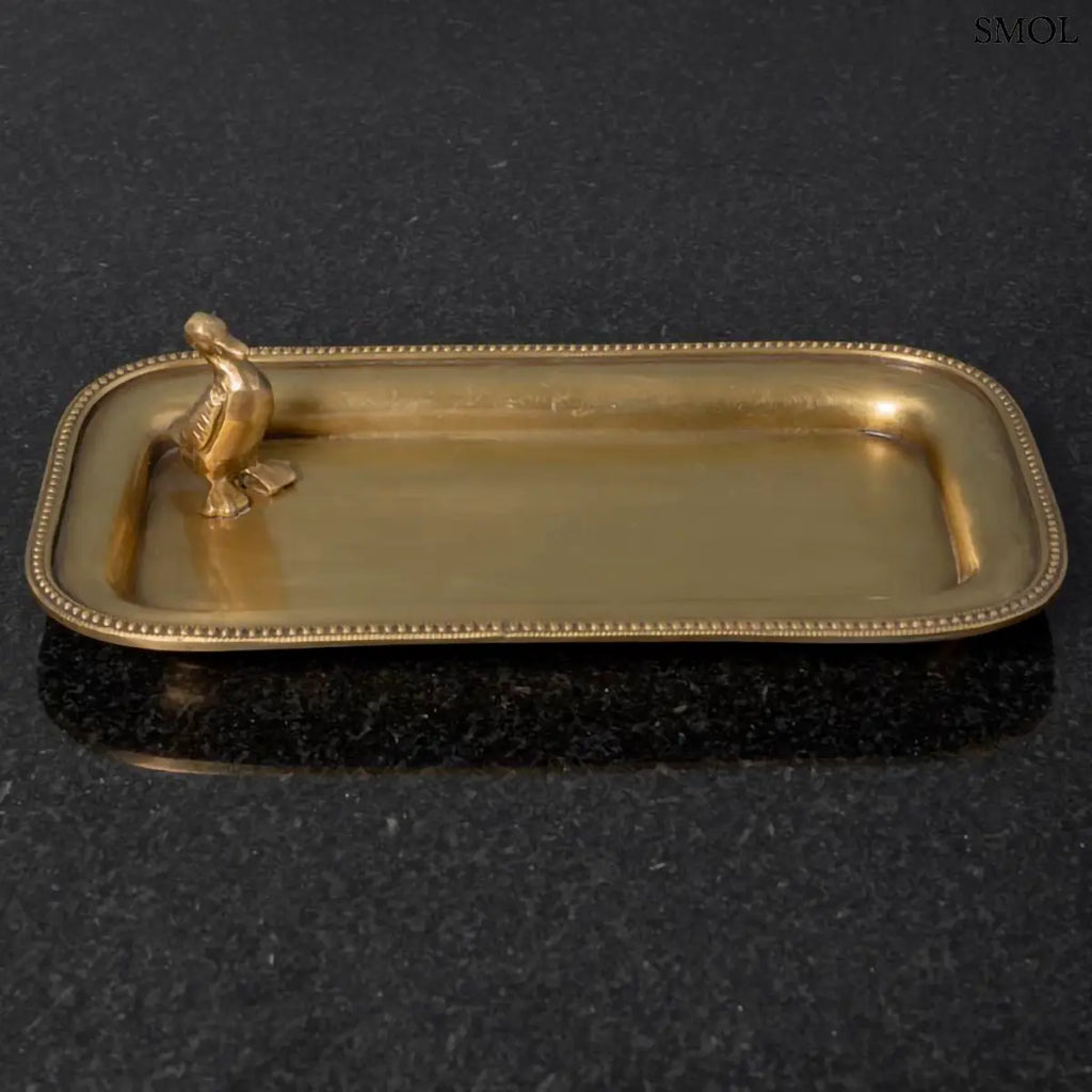 Antik arany sárgaréz dísztál ékszereknek, sarkában kis kacsa figurával, fekete háttérrel