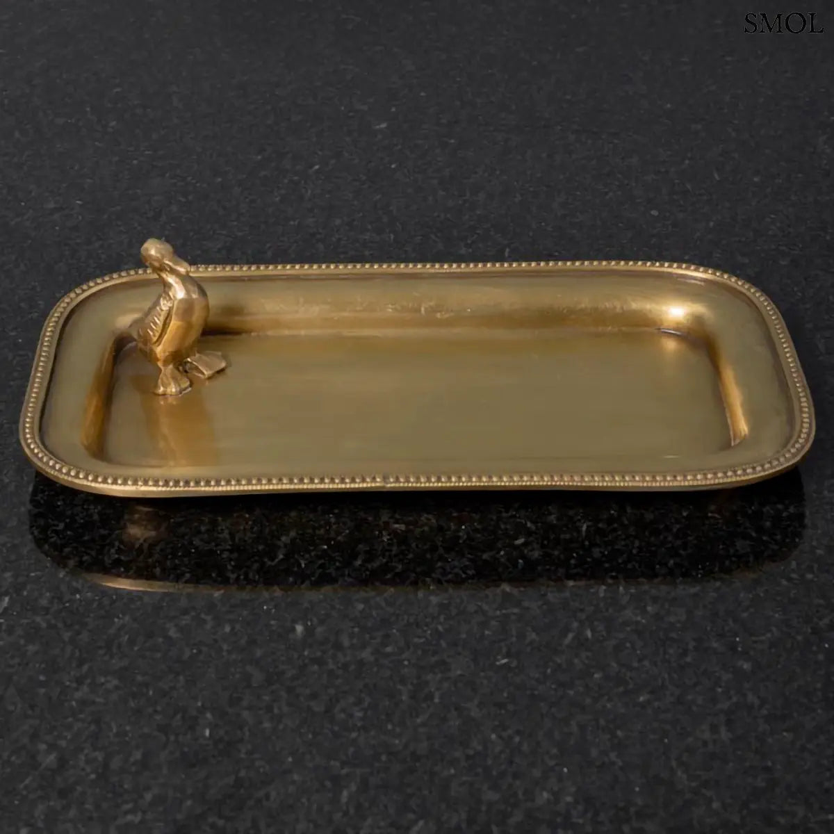 Antik arany sárgaréz dísztál ékszereknek, sarkában kis kacsa figurával, fekete háttérrel