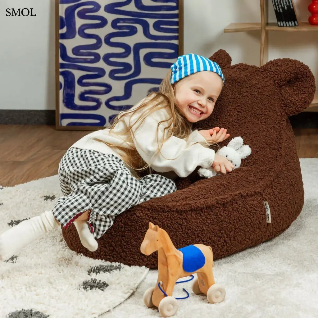 Barna színű, puha teddy anyagú gyerek babzsákfotel mackófülekkel, gyerekszobában, boldog gyerekkel