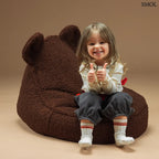 Barna színű, puha teddy anyagú gyerek babzsákfotel mackófülekkel, barna háttérrel, boldog gyerekkel