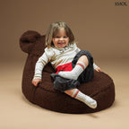 Barna színű, puha teddy anyagú gyerek babzsákfotel mackófülekkel, barna háttérrel, fekvő gyerekkel