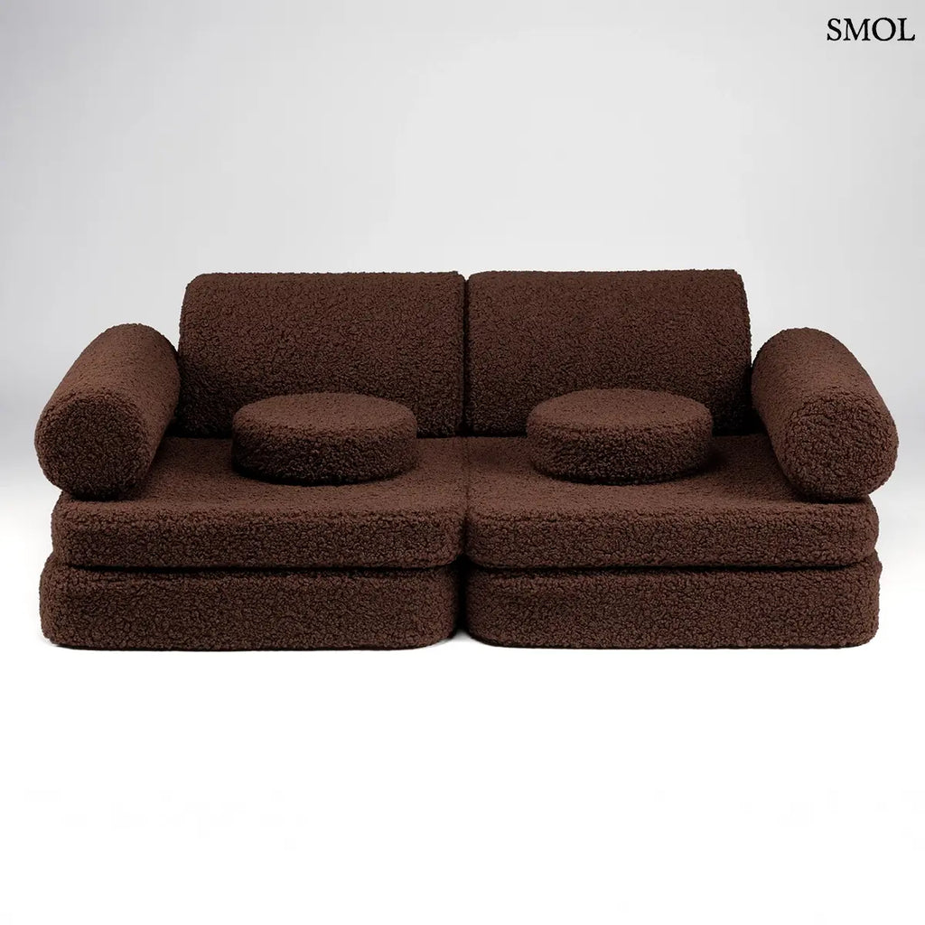 Barna, bársonyos tapintású kilencrészes gyerekkanapé henger és kerek párnákkal, puha teddy szövet borítással, szemből, fehér háttérrel