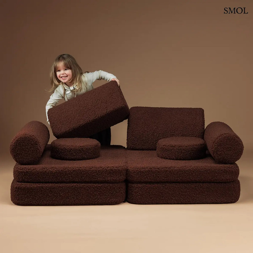 Barna, bársonyos tapintású kilencrészes gyerekkanapé henger és kerek párnákkal, puha teddy szövet borítással, háttámlával játszó gyerekkel