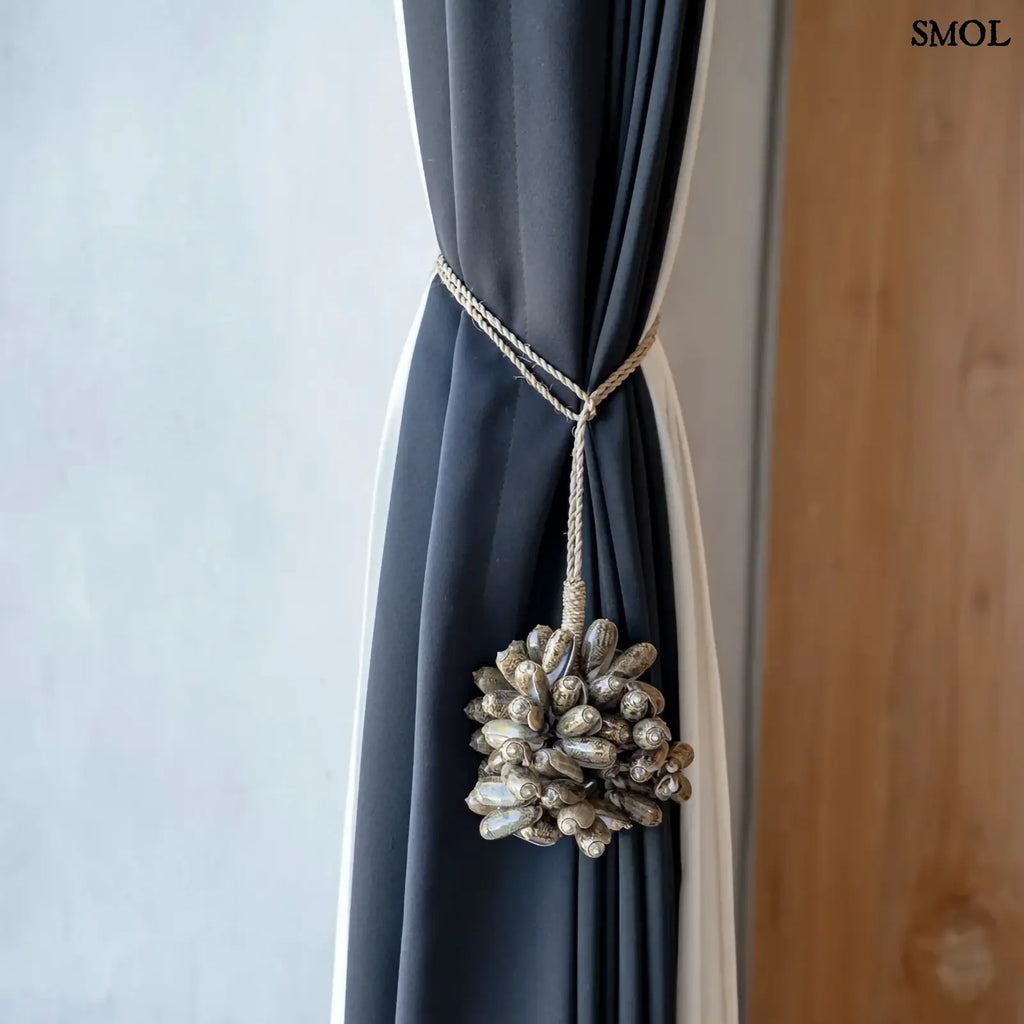 Barna kagyló függődísz, kézműves bojt formában, natúr kötélre akasztva függönyön