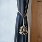 Barna kagyló függődísz, kézműves bojt formában, natúr kötélre akasztva függönyön