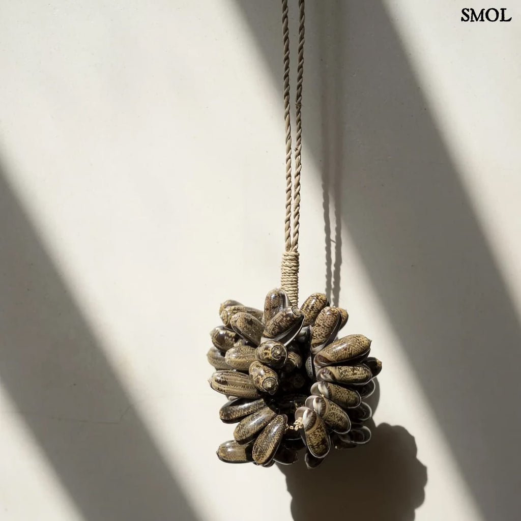 Barna kagyló függődísz, kézműves bojt formában, natúr kötélre akasztva falnál