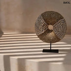 Natúr fehér kagylókból készült, kör alakú kagyló dekoráció fekete fémállvánnyal natúr háttérrel