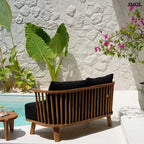 Kétszemélyes kanapé, újrahasznosított tíkfa kerettel és fekete kárpit párnákkal, teraszon, hátulról