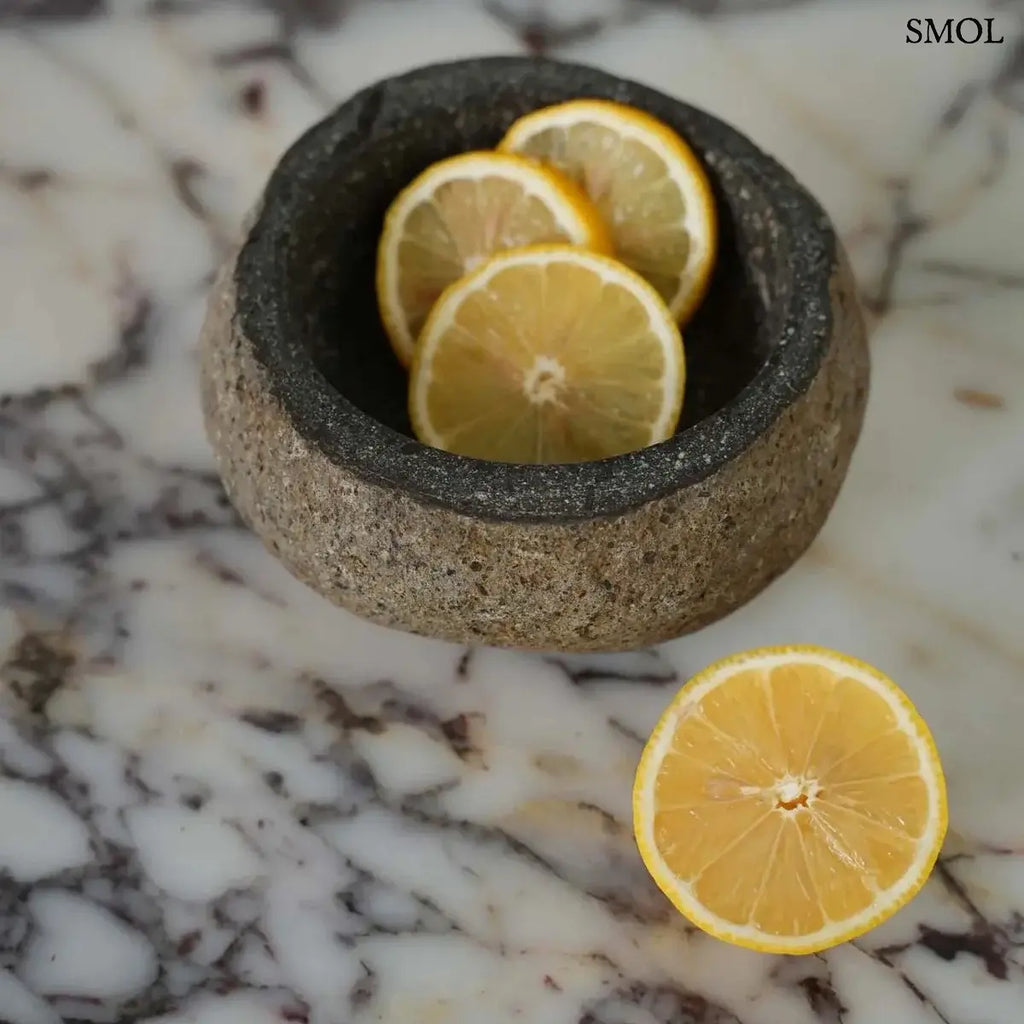 Rusztikus fekete lávakő tál kívül durva, belül csiszolt textúrával, természetes vulkanikus kőből, citrommal