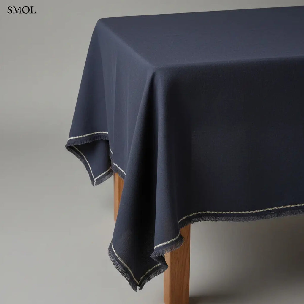 Lenvászon asztalterítő sötétkék/fekete színben, finom rojtozott szegéllyel és fehér dísztűzéssel, asztalon, ferdén