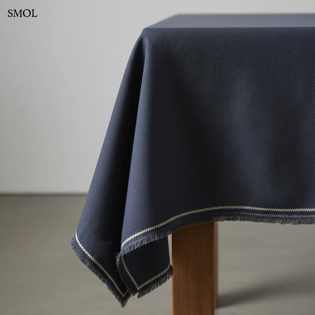 Lenvászon asztalterítő sötétkék/fekete színben, finom rojtozott szegéllyel és fehér dísztűzéssel, asztalon, oldalról