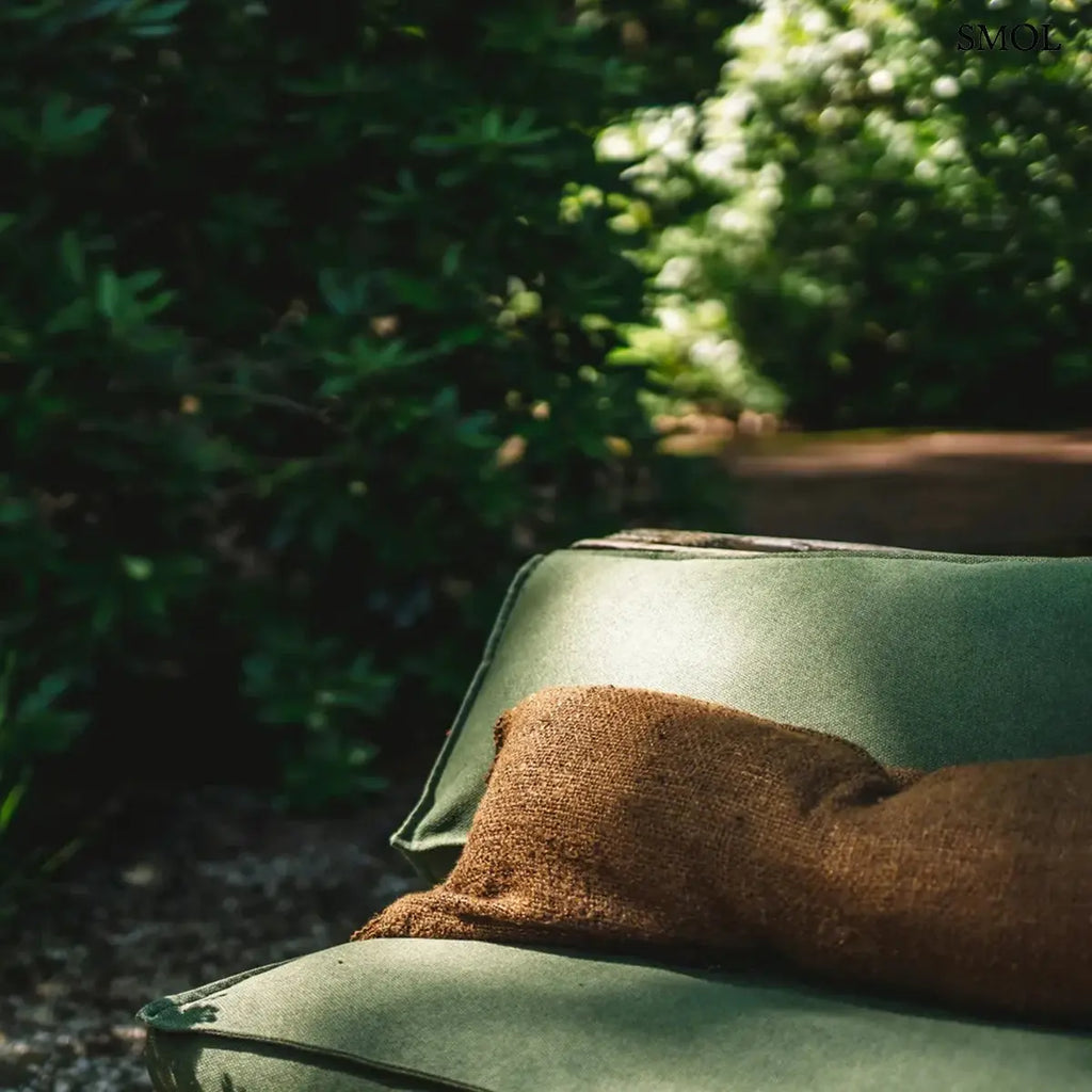 Hosszúkás, barna színű pamut díszpárnahuzat rojtos szélekkel és rusztikus szövéssel, zöld kanapén