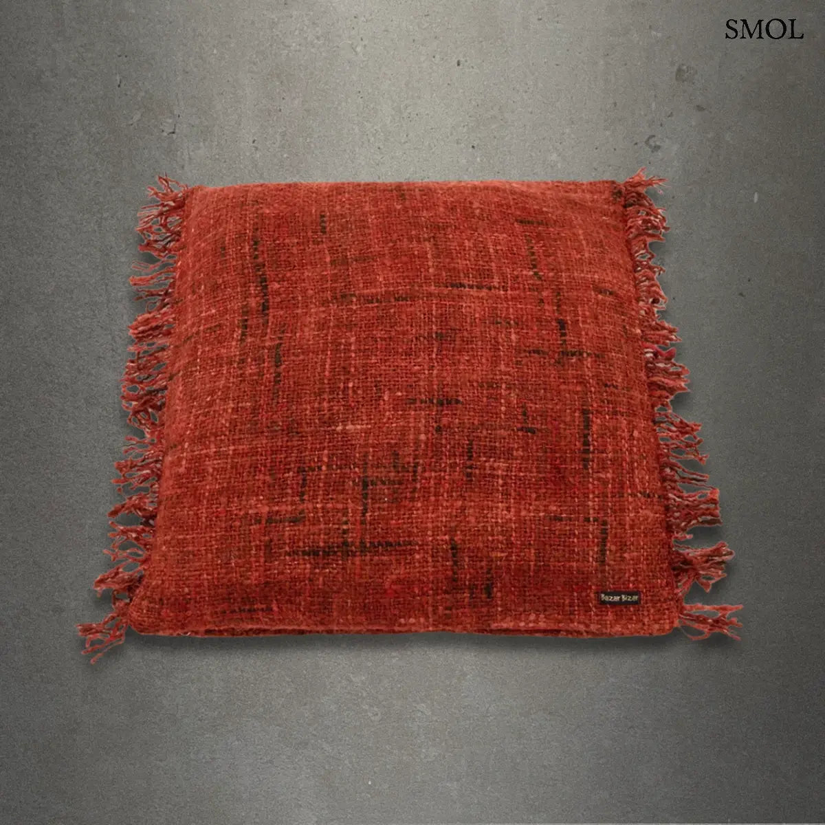 Bohém stílusú, kézzel szőtt cseresznyepiros pamut díszpárnahuzat rojtos szegéllyel, 60x60 cm-es méretben, szürke háttérrel