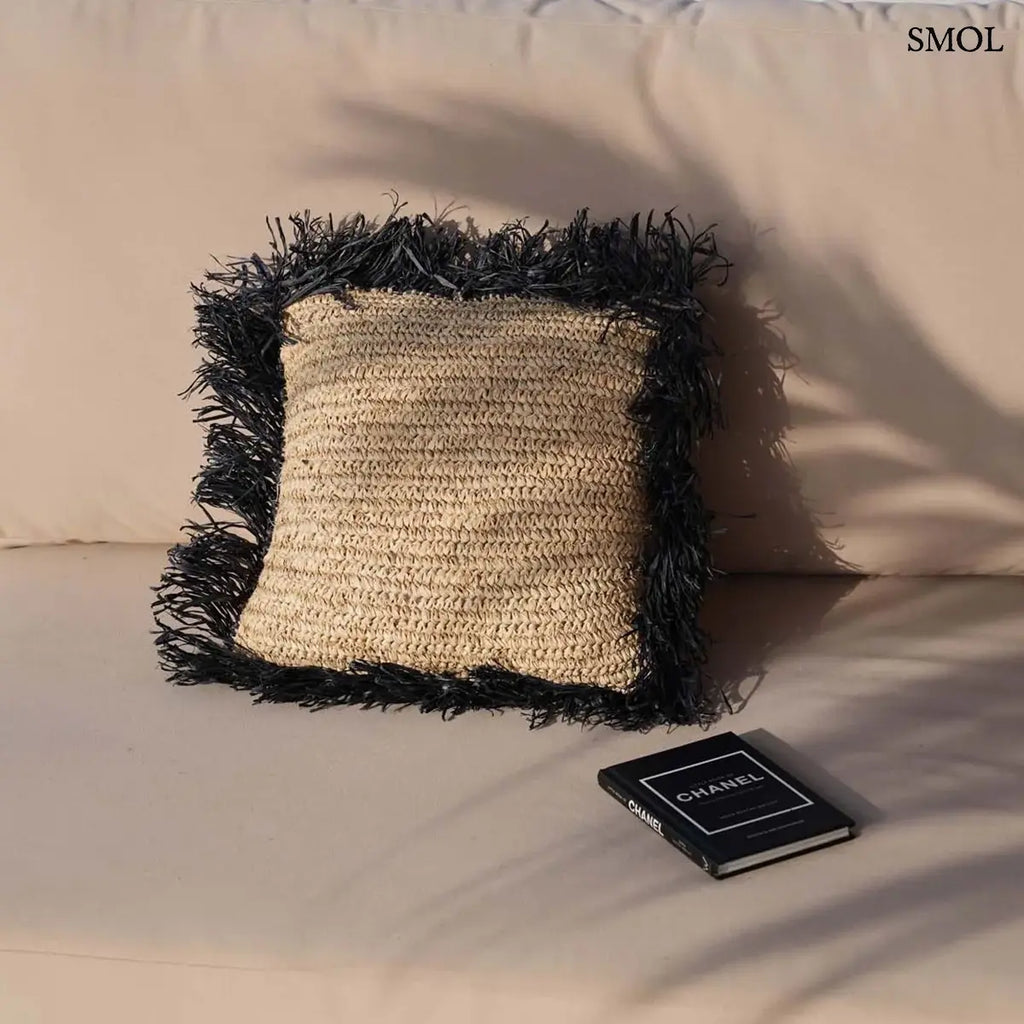 Fekete négyzetes raffia díszpárnahuzat 40×40 cm, természetes rostokkal, kanapén, szemből, könyvvel