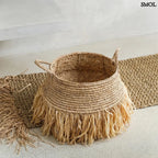 Raffia tárolókosár natúr színben, rojtos boho díszítéssel, padlón