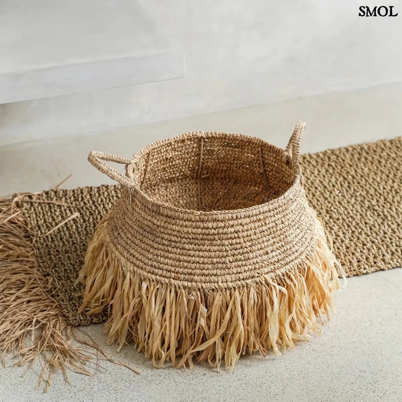 Raffia tárolókosár natúr színben, rojtos boho díszítéssel, padlón