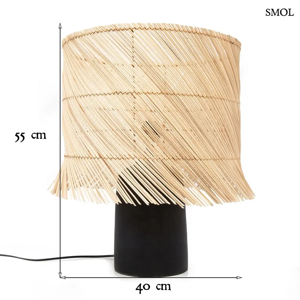 Modern asztali lámpa hengeres, fekete terrakotta talppal és natúr, ferdén szőtt rattan búrával, amelynek alsó széle játékosan rojtozott, méretekkel