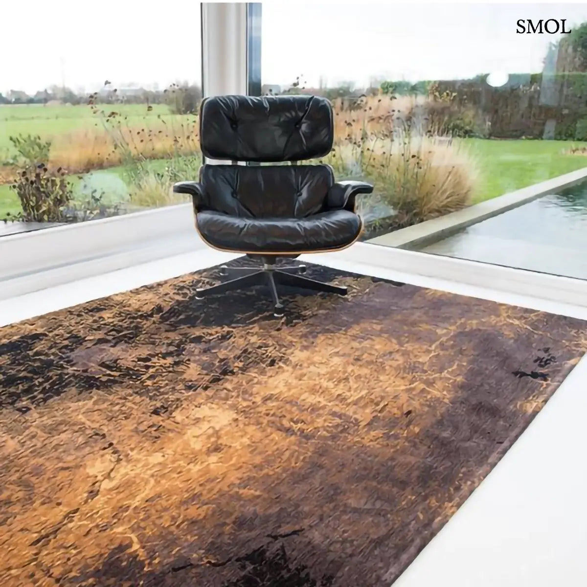 ECO RUG DEEP MINE absztrakt szőnyeg arany-barna kombinációban, négyzet alakú, repedezett, karcos felülettel, fotellel, medencével háttérben