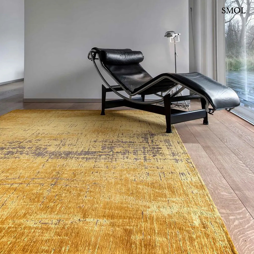 ECO RUG LIBERTY GOLD szőnyeg, aranyszín alapon sötétbarna és fekete festékszerű vonalakkal, action painting hatású mintázattal, távolabbról, fotellel