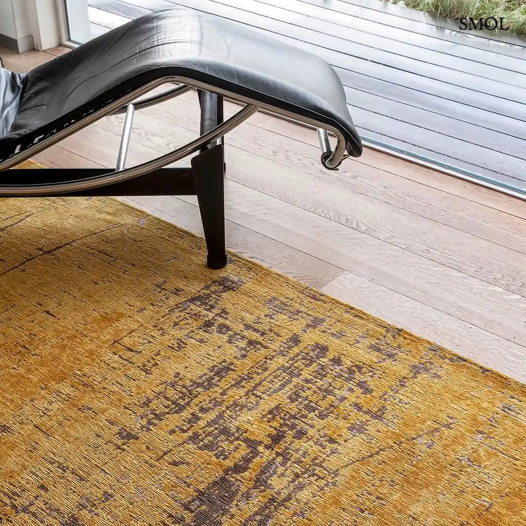 ECO RUG LIBERTY GOLD szőnyeg, aranyszín alapon sötétbarna és fekete festékszerű vonalakkal, action painting hatású mintázattal, fotellel közelről nagyítva