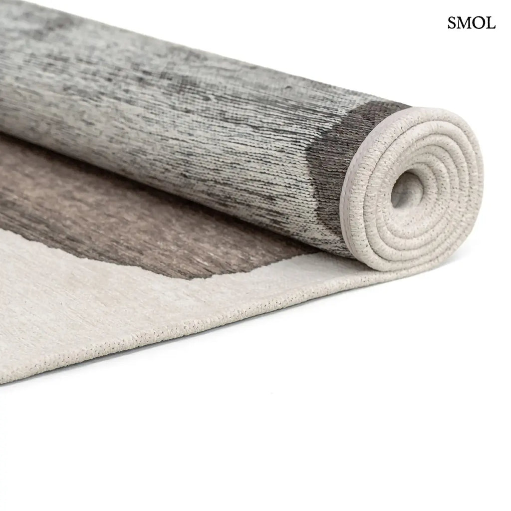 ECO RUG MASTIC absztrakt szőnyeg fehér alapon taupe-barna vízszintes rétegű festői mintával, feltekerve