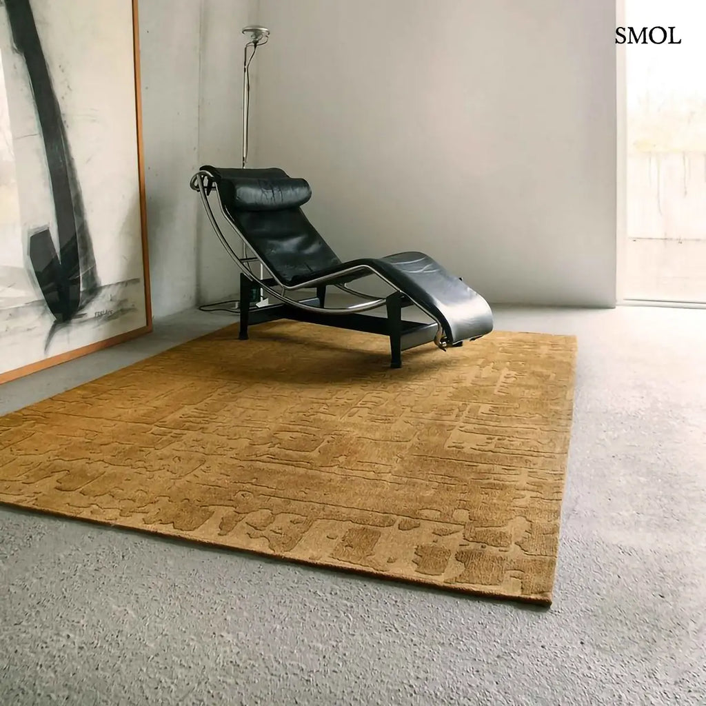 ECO RUG MADAGASCAR GOLD baobab mintás szőnyeg arany-mustár tónusokban, kéregszerű afrikai textúrával, fekete fotellel, oldalról