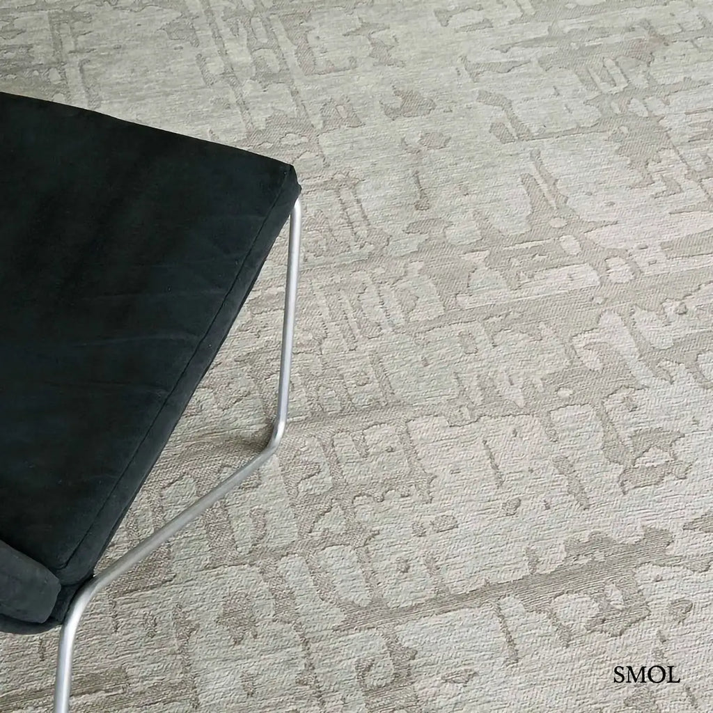 ECO RUG DRY BEIGE baobab mintás szőnyeg bézs-szürke tónusokban, halvány kéregszerű afrikai textúrával, fotellel, nagyítva