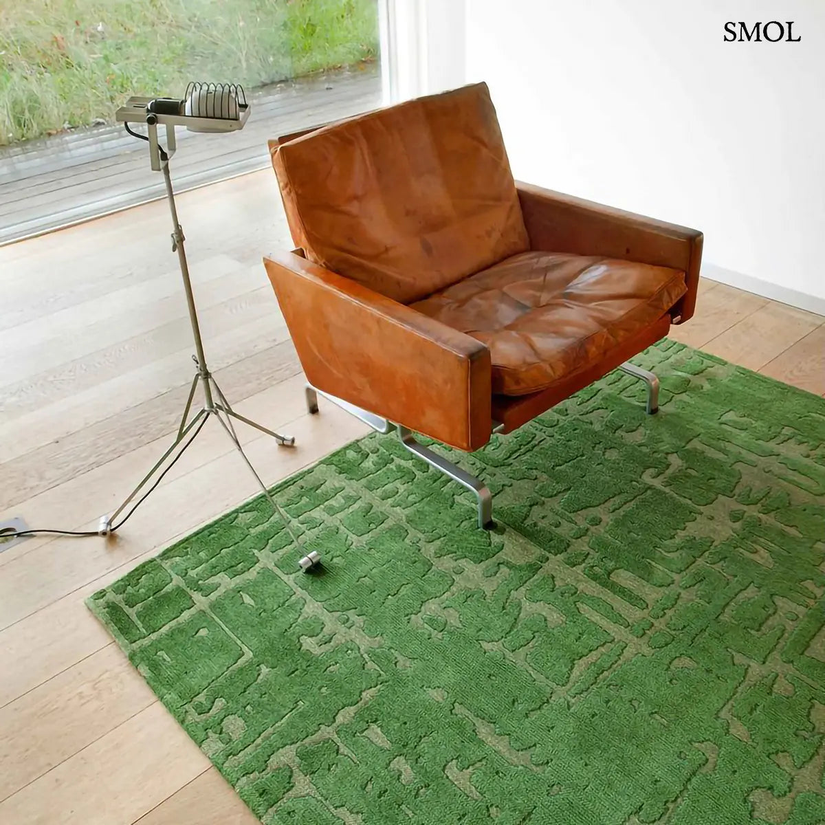 ECO RUG PERRIER'S GREEN szőnyeg, zöld alapon halványabb, repedezett baobab mintázattal, szabálytalan vonalvezetéssel, barna fotellel