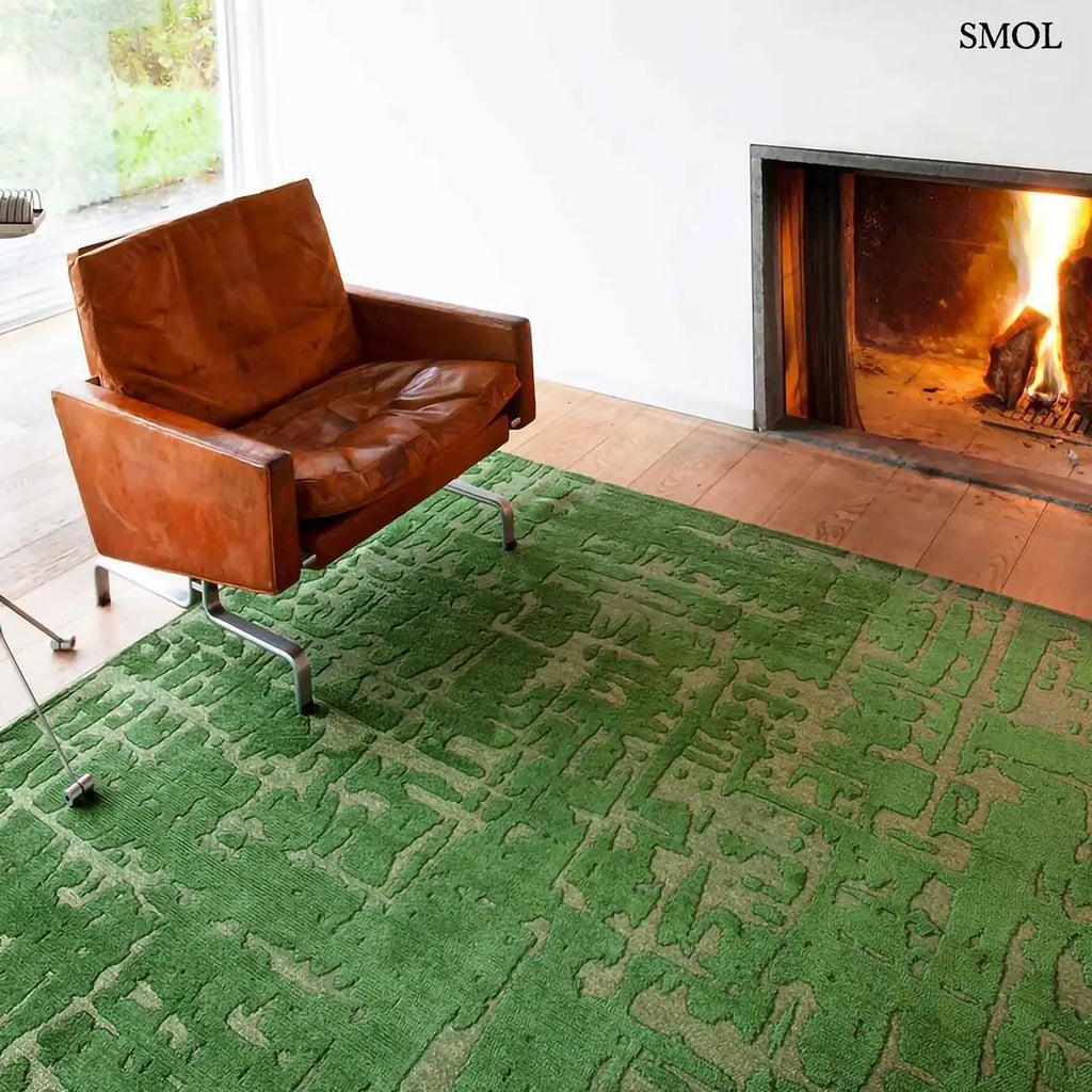 ECO RUG PERRIER'S GREEN szőnyeg, zöld alapon halványabb, repedezett baobab mintázattal, szabálytalan vonalvezetéssel, barna fotellel és kandallóval