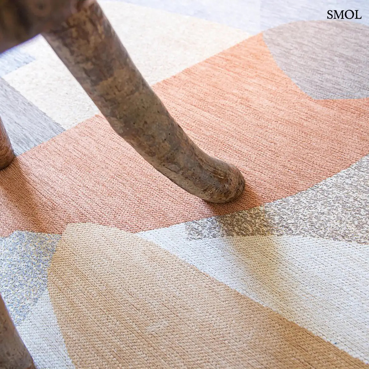 ECO RUG SECRET szőnyeg, narancs, kék, szürke és bézs geometrikus formákból összeálló, egymásba fonódó mintázattal, falábbal, nagyítva