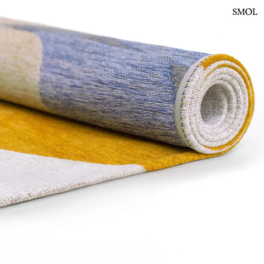 ECO RUG SUNNY BLUE szőnyeg, kék, sárga és barna kavicsszerű formákból álló, egymást átfedő mintázattal, feltekerve