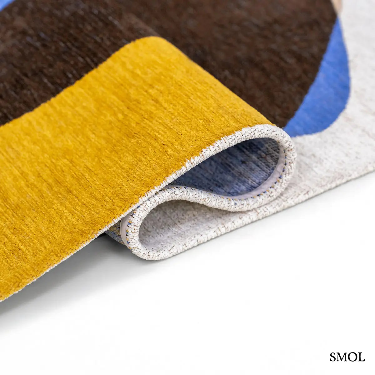 ECO RUG SUNNY BLUE szőnyeg, kék, sárga és barna kavicsszerű formákból álló, egymást átfedő mintázattal, hullámosra hajtogatva