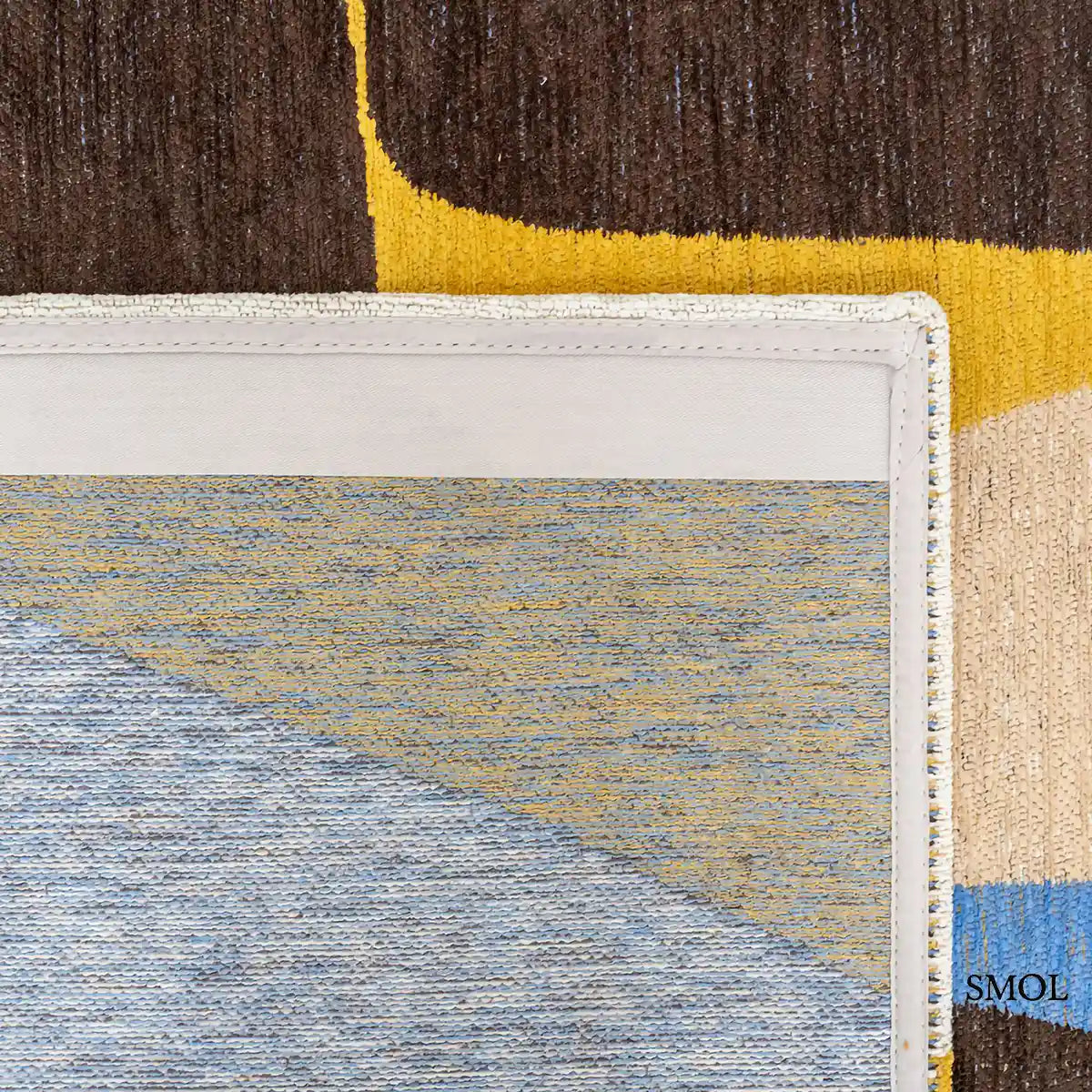 ECO RUG SUNNY BLUE szőnyeg, kék, sárga és barna kavicsszerű formákból álló, egymást átfedő mintázattal, felhajtott sarokkal, alulról