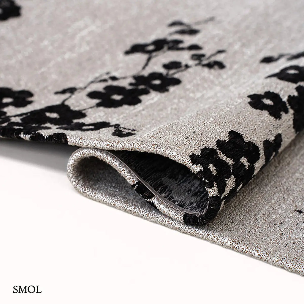 ECO RUG NIGHT SNOW sakura mintás szőnyeg világos alapon, fekete cseresznyevirág motívumokkal, hullámosan hajtogatva
