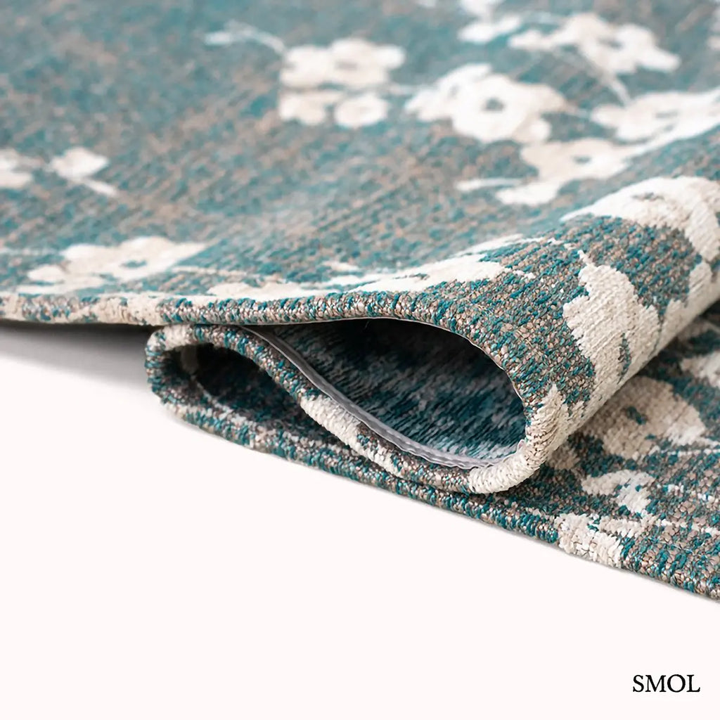 ECO RUG LAKE BLUE sakura mintás szőnyeg türkizkék alapon fehér-krém cseresznyevirág ágakkal, hullámosra hajtogatva