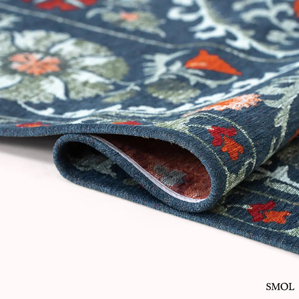 ECO RUG NORDIC suzani mintás szőnyeg sötétkék alapon narancs, piros és zöld virágmotívumokkal, hullámosra hajtogatva
