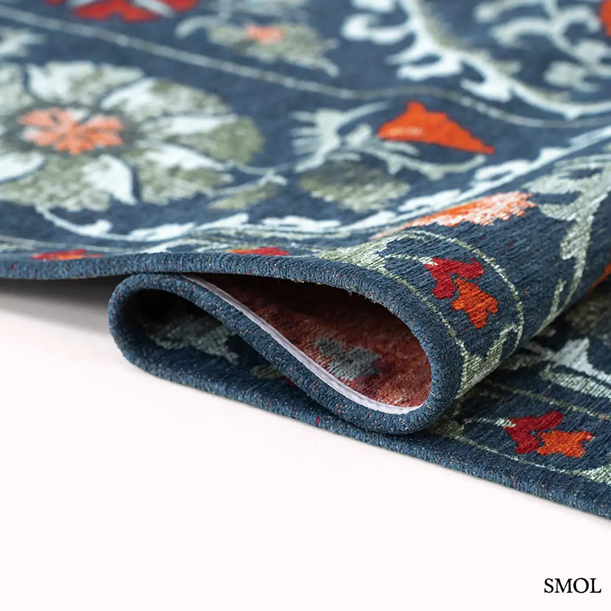 ECO RUG NORDIC suzani mintás szőnyeg sötétkék alapon narancs, piros és zöld virágmotívumokkal, hullámosra hajtogatva