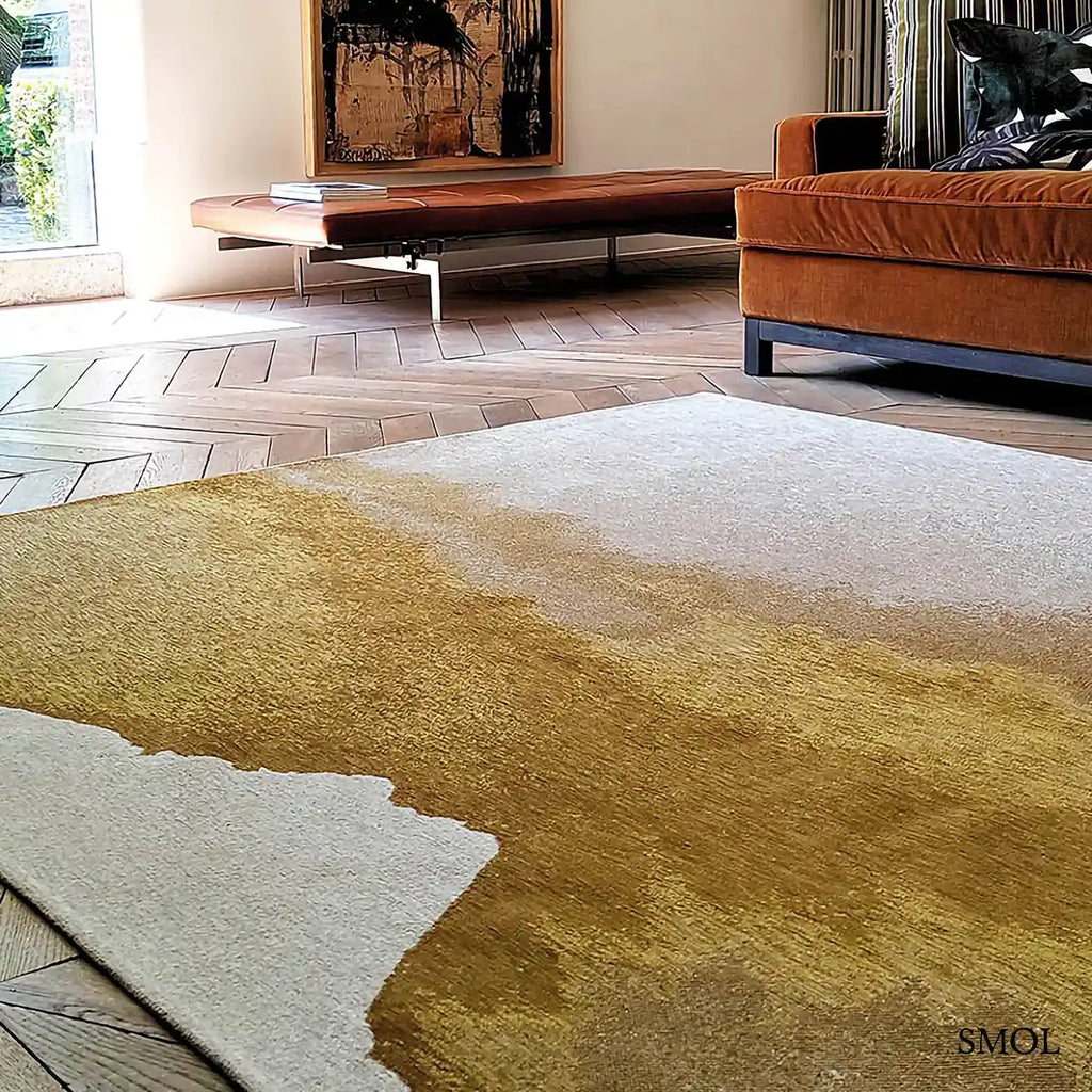 ECO RUG SUNSET szőnyeg, arany és barna színátmenettel, egyik oldalon világosabb szürkés tónusba mosódó tintafolt mintázattal, nappaliban