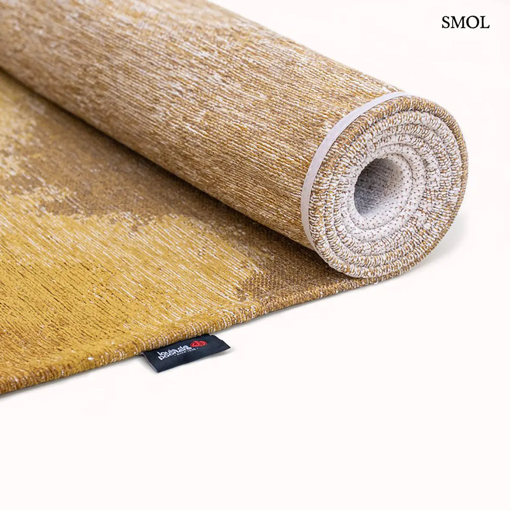 ECO RUG SUNSET szőnyeg, arany és barna színátmenettel, egyik oldalon világosabb szürkés tónusba mosódó tintafolt mintázattal, feltekerve