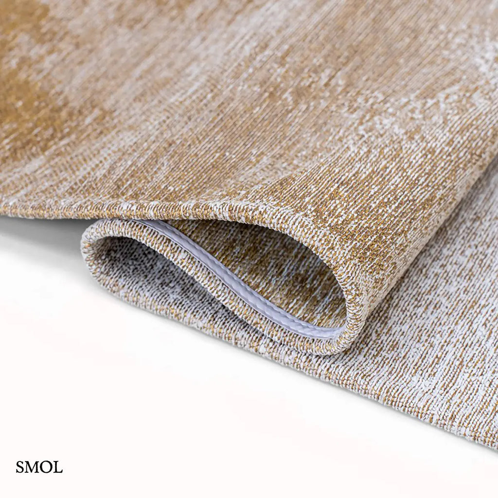 ECO RUG SUNSET szőnyeg, arany és barna színátmenettel, egyik oldalon világosabb szürkés tónusba mosódó tintafolt mintázattal, hullámosra hajtogatva