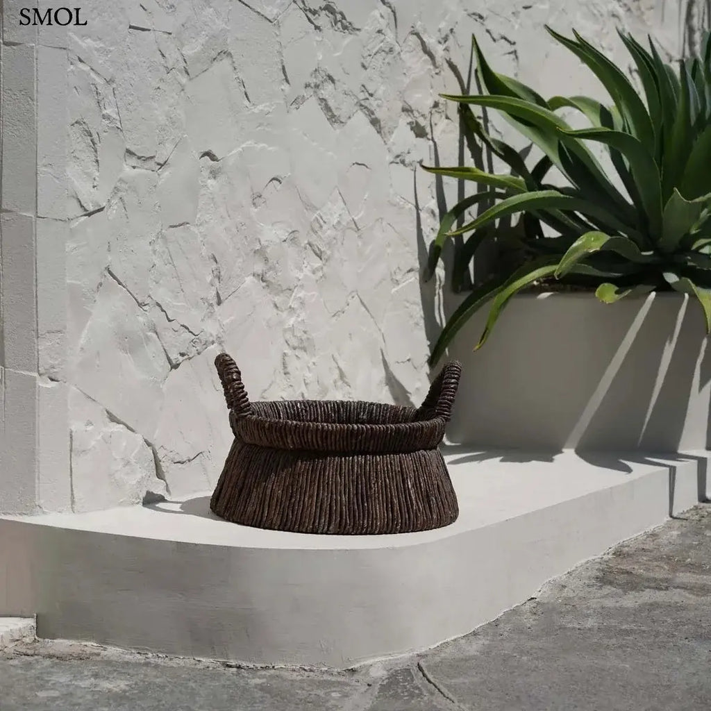 Kézzel font, sötétbarna banánlevél tárolókosár felfelé szűkülő háromszög alakú dizájnnal és masszív fogantyúkkal, kültéren