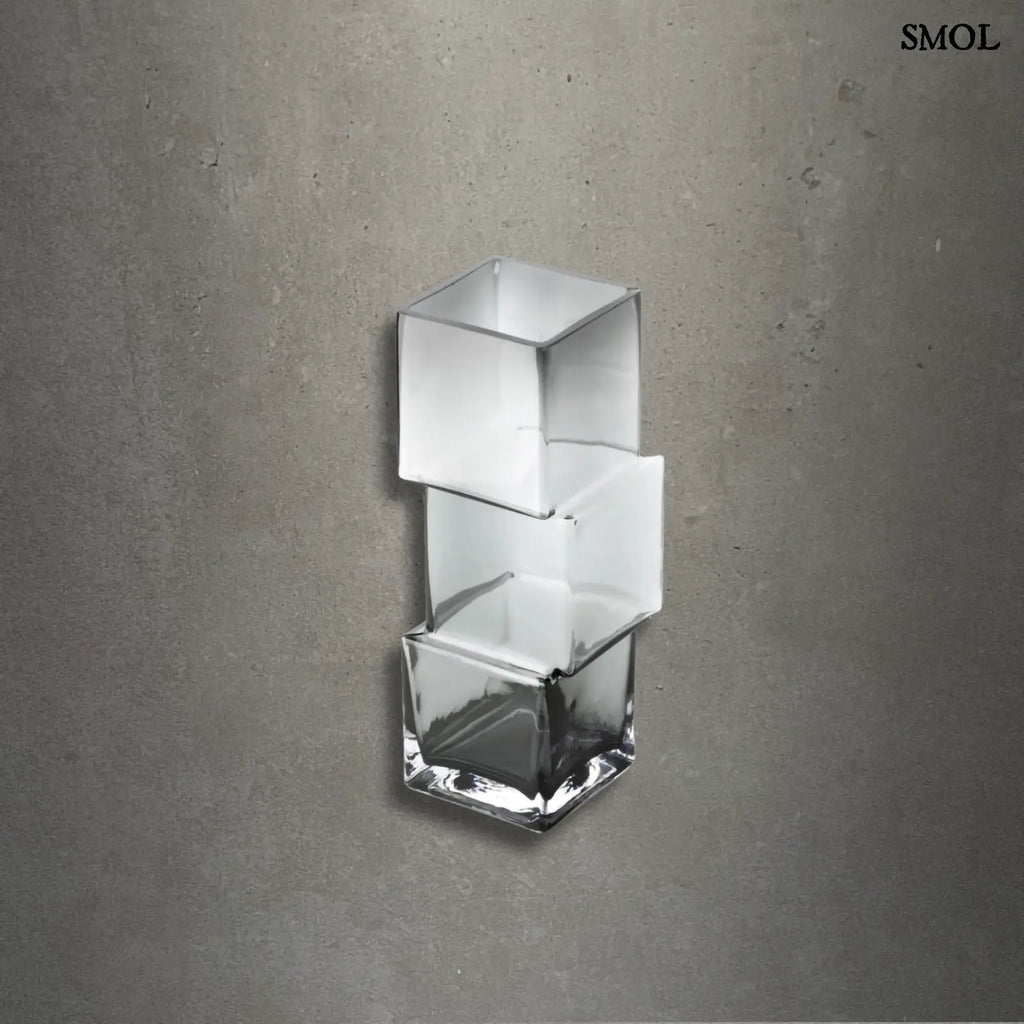 Függőlegesen elrendezett, három kocka alakú sötétszürke üveg váza, szürke háttérrel