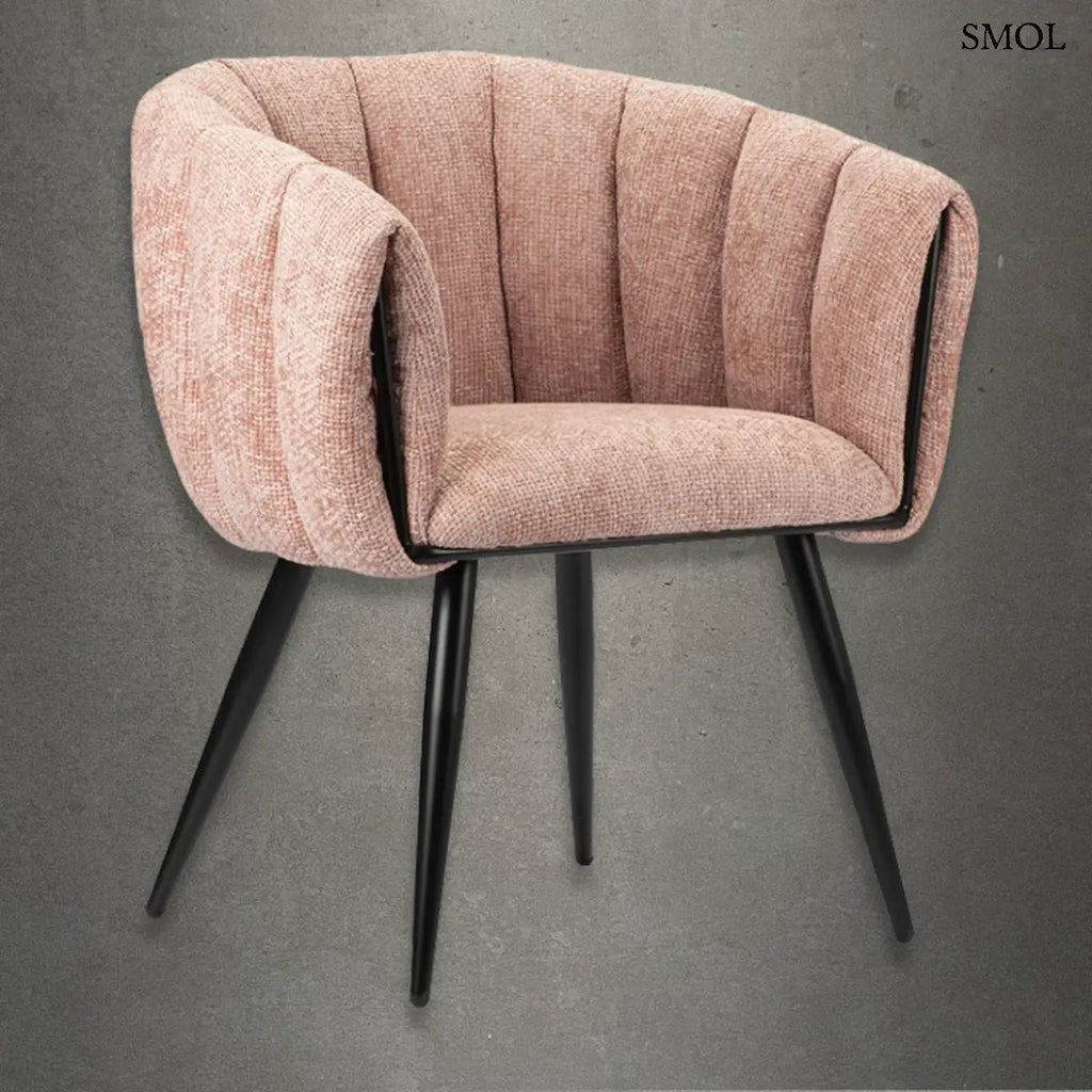 Modern, kagylóformájú étkezőszék függőlegesen tűzött, púderrózsaszín kárpitozással és karcsú, fekete fém lábakkal, szürke betonhatású háttér előtt.