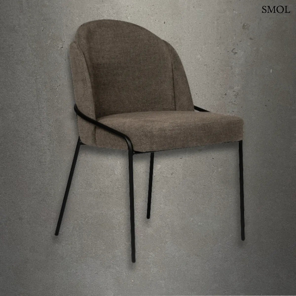 Taupe színű, kárpitozott FJORD étkezőszék texturált szövettel, ergonomikus háttámlával és vékony, fekete fém lábakkal, beton hatású háttér előtt.